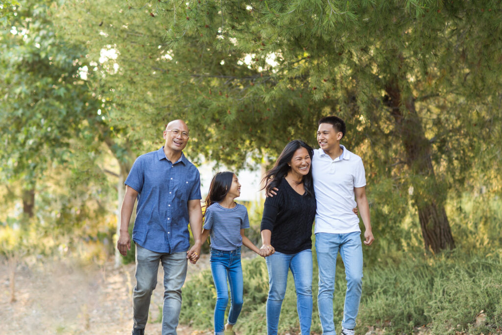 A family of four holding hands as they walk through a park with trees surrounding them