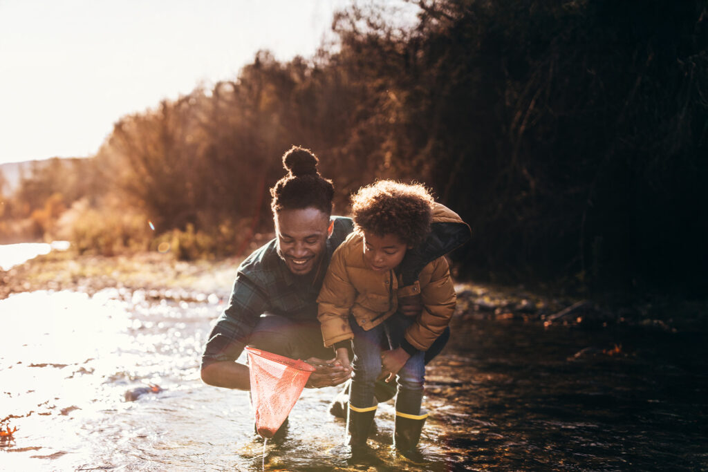 A father and his son in a lake with a net, looking at something they caught